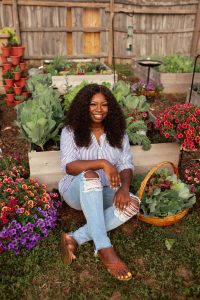 Jasmine Jefferson of Black Girls With Gardens sat smiling surrounded by flowers and planters