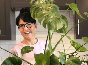 Ellen Mary of Ellen Mary gardening smiling behind tall house plant
