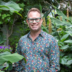 Dan Cooper in a patterned shirt smiling stood among plants