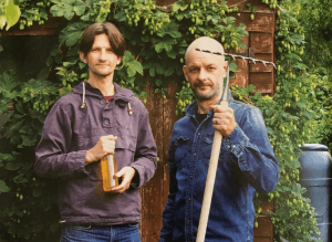 Nick Moyle and Richard Hood of Two Thirsty Gardeners holding a rake and a bottle